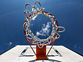 Der Blick auf einen Basketballkorb bei strahlend blauem Himmel und ein paar Wolken an einem sonnigen Tag zeigt die Freude am Sport im Freien.