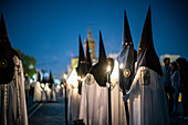 Nazarenos from the Estrella brotherhood walk with candles in the night of Palm Sunday, celebrating Holy Week in Seville.