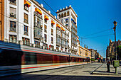 Located in Seville, the Aurora Building showcases regionalist architecture amidst a vibrant urban street scene with a passing tram.