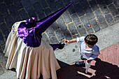A nazareno hands a religious card of the Virgin to a boy while participating in Holy Week festivities in Seville, Spain.