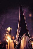 A nighttime procession featuring penitents with traditional outfits holding candles during Holy Week.