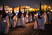 Nazarenos from the Estrella brotherhood walk with candles in the night of Palm Sunday, celebrating Holy Week in Seville.