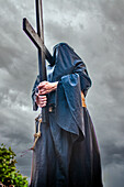A hooded penitent solemnly carries a wooden cross in Seville, celebrating the deeply rooted traditions of Holy Week in Andalusia.