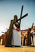 During Holy Week in Seville, penitents from the Hermandad de Santa Genoveva solemnly carry wooden crosses as a sign of faith.
