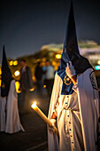 A nighttime procession featuring penitents with traditional outfits holding candles during Holy Week.