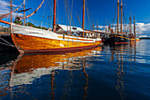 Boote und Segelschiffe liegen friedlich am Aker Brygge Dock in Oslo und reflektieren das warme Sonnenlicht auf dem ruhigen Wasser.