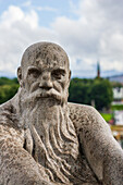 Intricate sculpture in Vigeland park captures a contemplative figure surrounded by lush greenery in Oslo, Norway on a sunny day.