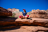 Junge kaukasische Frau sitzt mit gekreuzten Beinen auf dem Canyon Overlook Trail im Zion National Park, Utah