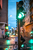 City street at twilight featuring a glowing green traffic light and blurred movements.