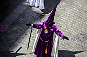 Holy Week tradition in Spain featuring cloaked penitent during a religious procession.