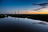Soft hues of dusk illuminate the irrigation channels of Doñana, creating a tranquil reflection in the still waters as day fades.