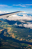 Soaring above Oslo, Norway, admire lush green valleys and shimmering waterways beneath clear skies and fluffy clouds during summer.