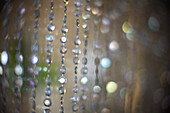 Intricate beaded glass curtain displays delicate patterns in soft focus, highlighting a captivating ambiance and shimmering bokeh.