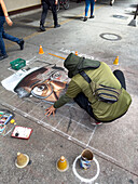 An artist drawing a portrait with chalk on the sidewalk in downtown Medellin, Colombia.
