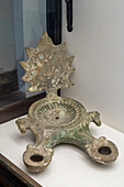 A large oil lamp with two nozzles in the Vesuvian Life Gallery, National Archaeological Museum of Naples, Naples, Italy. The lead-glazed terra cotta lamp is decorated with a vine leaf and horse heads. From Pompeii, circa 1st Century A.D.