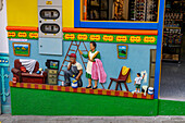 Colorfully-painted woodwork & humorous 3-D plaster mural or zócalo on the wall of a shop in Guatape, Colombia.