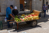 A man buying produce from a street vendor with a mobile cart in Rionegro, Colombia.