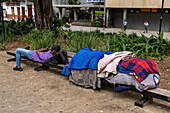 A homeless person sleeping on a park bench with his belongings in Bolivar Park in Medellin, Colombia.