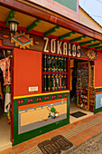 Colorfully-painted woodwork and a humorous plaster mural or zócalo on the wall of a shop in Guatape, Colombia.