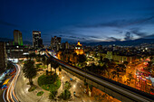 Evening twilight in Medellin, Colombia, with the Palace of Culture at center. A long exposure produces streaking lights from vehicles and a train.