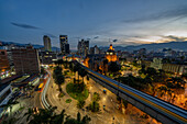 Evening twilight in Medellin, Colombia, with the Palace of Culture at center. A long exposure produces streaking lights from vehicles and a train.