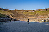 Tourists in the arena of the Amphitheater of Pompeii in the ancient Roman ruins of Pompeii in Italy.