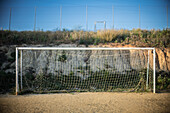 Ein Torpfosten steht auf einem unbefestigten Fußballplatz in Carrión de los Céspedes, über dem ein klarer Himmel und eine natürliche Kulisse aus trockenem Gras liegt.