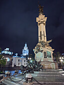 Nachtansicht des Unabhängigkeitsdenkmals auf der Plaza Grande in Quito, Ecuador, mit der Metropolitan-Kathedrale im Hintergrund.