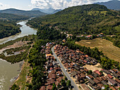 Luftaufnahme eines malerischen Dorfes an einem ruhigen Fluss, umgeben von üppigen Bergen und Ackerland, Bezirk Pak Ou, Luang Prabang, Laos.
