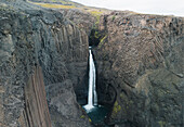 Aerial view of Studlafoss waterfall cascading over rugged basalt columns amidst pristine nature, Vatnajokull, Iceland.