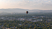 Luftaufnahme von bunten Heißluftballons über einer heiteren Stadtlandschaft mit Bergen und Bäumen, Reno, Nevada, Vereinigte Staaten.