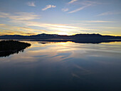 Aerial view of serene winter sunset over a tranquil lake reflecting majestic mountains and soft clouds, Glenbrook, Nevada, United States.