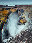 Luftaufnahme des majestätischen Dettifoss-Wasserfalls mit einem leuchtenden Regenbogen inmitten zerklüfteter Felsen und starkem Nebel, Vatnajokull, Island.