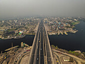 Luftaufnahme einer belebten Stadtlandschaft mit einer Brücke und einer Straße über einen Fluss, Darus Salam Thana, Dhaka, Bangladesch.
