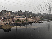 Luftaufnahme des Flusses Buriganga, umgeben von Industriegebäuden und Stromleitungen, Lalbagh Thana, Dhaka, Bangladesch.