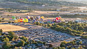 Aerial view of colorful hot air balloons over a vibrant landscape with a parking lot and trees, Old Northwest, Reno, Nevada, United States.