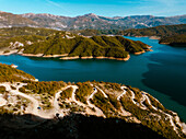 Aerial view of serene Bovilla Lake surrounded by majestic mountains and a winding road, Herraj, Tirana, Albania.