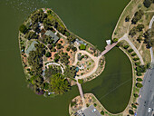 Aerial view of a picturesque lake surrounded by lush greenery, trees, and scenic pathways with a bridge, Da Lat, Lam Dong, Vietnam.