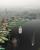 Aerial view of boats on the Buriganga river near cement industries in a bustling cityscape, Amin Bazar, Savar, Dhaka, Bangladesh.
