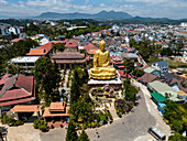 Luftaufnahme einer goldenen Buddha-Statue und eines traditionellen Tempels, umgeben von ruhigen Gärten und einer lebendigen Stadtlandschaft, Bezirk 8, Da Lat, Lam Dong, Vietnam.