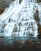 Aerial view of dynjandi waterfall with a girl beside the pool and rugged rocks, Westfjords, Iceland.
