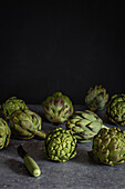 Fresh artichokes, skilfully arranged on a dark, textured surface, ideal for culinary and healthy living concepts. The contrast emphasises their rich green tones.