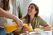 A lesbian couple enjoy a casual breakfast at home A woman smiles warmly as her partner pours her fresh orange juice, creating a moment of connection and love