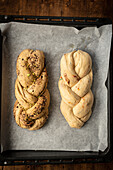 Top view of freshly baked bakbah loaves on parchment paper. One loaf is topped with pistachios and spices, the other with chocolate.