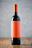 A single wine bottle with a simple orange label on a wooden table against a grey background, ideal for branding mockups.