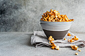 Grey bowl of sweet caramel popcorn on textured linen against a grey background to highlight the rich, golden hues of the snack.