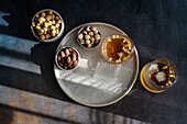 Top view of a richly flavoured cognac cocktail with cinnamon, aniseed star and various nuts such as almonds, peanuts and hazelnuts, elegantly presented on a textured tray.