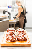 A display of freshly baked Italian pastries sprinkled with sugar crystals on a wooden board A baker works in the blurred background, creating a cosy bakery atmosphere