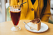 A cosy café scene with a refreshing iced coffee in a tall glass and a delicious piece of chocolate cake on a white plate, on a wooden table with a warm ambience