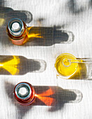 Top view of natural body oils infused with plants such as calendula and rose. The image captures the bright colours of the oils in glass bottles that cast shadows.